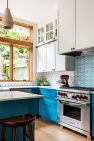 A high-end, light-filled kitchen with blue base cabinets, white upper cabinets, tile backsplash, and a Wolf range.