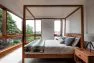 A master bedroom with a modern canopy bed made of wood and large windows.