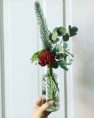 A glass bottle vase with a floral arrangement of greenery and one flower.