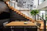 View of the clubroom amenity space at the Lucille on Roosevelt, where a dining table is nestled into the bend of a staircase made of heavy timber.