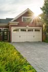The sun flares over the roof of a Craftsman garage painted red with white trim.
