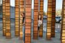 Brie and a friend peek out from behind an art installation near Seattle Center. The installation looks like bamboo, with brown, flat, vertical pillars shooting up with horizontal black stripes on them.