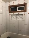 A work-in-progress shower with 1' by 2' white tiles being installed. There are spacers in place to keep the tiles from shifting as they set.