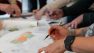 A close-up shot of a table covered in papers with the hands of people marking them up.