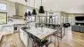 Looking into a kitchen and the great room beyond. A kitchen island is the the foreground. There are abundant windows and the room is bright.