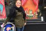 Lindsey stands outside a shop window smiling for the camera with her son in his stroller. The window has a bright orange display in it.