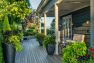 Looking across the deck toward to valley-view below. The sun hangs low in the sky casting light and shadow across the deck. Charcoal-colored planters lining the deck overflow with green, purple, and magenta plants. – Residential landscape by Board & Vellum