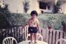 A small Sneha stands on a small, white, round table outside her childhood home.