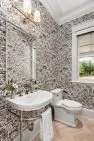 A small bathroom with a while sink and toilet. The walls are covered in a wallpaper with a busy building print. The buildings on the wallpaper are overlapping and in the style of an old European city.