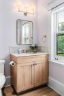 A small bathroom vanity made in light wood with dark purple cabinet pulls. The walls are light purple.