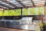 A covered outdoor kitchen features stainless steel counters and storage, a grill and a smoker. - Backyard Covered Kitchen – Board & Vellum