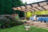 A large canopy covers a deck with an outdoor kitchen, hot tub, and shower. - Backyard Covered Kitchen – Board & Vellum