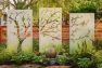 Within a green and lush garden stands a custom outdoor art piece – a triptych showing a tree with its branches extending to the right. The tree is a cutout and you can see through to the yard behind the art.