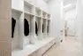 To the left, a large bank of white cubbies and drawers create bench seating. There are black coats hanging on the cubbies.