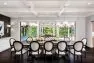 Looking toward three French doors, all open. In front is a large table with twelve upholstered seats around it. Beyond is a deck with additional seating.