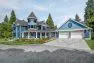 Outside a large, new home, which is blue in color with a large, two car garage, gables, and a large turret.