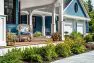 A wrap around deck with wicker rocking chairs. In front are blooming spring flowers. On the deck, potted plants bring the landscape up to the human-level.