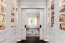 A large hallway lined with built-in shelving full of books ends in a set of pocket doors, behind which is a study.
