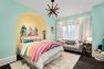 A mint green kids room with a large, inset arch painted pale yellow. The bed is tucked under the arch with a surfboard-like headboard. There is a couch and lots of toy storage.