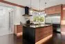 A large kitchen island stands front and center. Behind is a navy blue range and hood. Above the island are glass pendants.