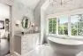 A gray and white bathroom with a large soaking tub, built-in vanity and sink, and tiled floor.