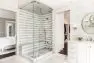 At the center stands a large shower stall with clear glass doors. The shower stall is tiled in striped grey and white.