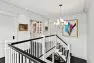 A view of the bright white upstairs hallway at the Snohomish Estate, looking toward an illuminated built-in library. The formal dining room is just visible below the stairs.