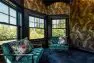 The Snohomish Estate turret loft with teal green tufted chairs, royal blue carpet, and gold wallpaper with a peacock motif.