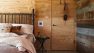 A bedroom with plywood and reclaimed wood walls. There is a bed to the left with pink sheets.