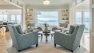 Four chairs encircle a round coffee table. In the background, a large window looking out at Puget Sound is flanked by two built in book cases.