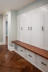 White storage cabinets with a dark wood bench for seating.