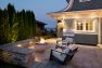 Free-standing and build-in seating surround a fire pit nestled behind a house.