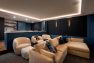 A home theater with dark blue walls and cream colored sofas and chairs.