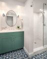 A brightly lit bathroom with sage green cabinets and geometric floor tiling. A tiled shower is to the right.