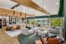 A photo of the interior of a multifamily residential amenity clubhouse with vaulted ceilings framed with wide wooden beams. Presents a wide view of the room to show how it has been furnished into several zones with different purposes such as conversation, working, dining, and relaxing.