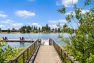 A photo of a wooden dock stretching out over landscaping and foliage at the edge of a lake. Includes a floating dock with deck chairs and a ladder for swimmers.