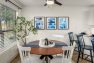 A photo of the interior of an apartment dining room. Focuses on a round wood dining table and four white spindle dining chairs. Includes a houseplant and blue abstract art on the walls.