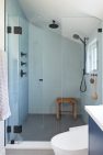 An interior view of a modern bathroom with a walk-in shower that is fully tiled and enclosed with a frameless glass door, with a wooden bath stool in the corner. Judkins Park Victorian – Board & Vellum