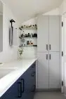 An interior view of a modern bathroom showing a long horizontal vanity with a stone countertop, with tile laid in a grid on the floor and the wall. There is also a tall storage cabinet with four doors and wall mounted glass shelving. Judkins Park Victorian – Board & Vellum