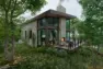 An architectural rendering of a cabin-style vacation rental home. The cabin has full-height windows, a large fireplace, and a deck.