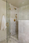 A cream tiled shower with a glass door.