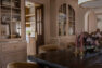 A formal dining room with a large dark wood dining table surrounded by brown suede chairs. Built in cabinetry in a dusty pink lines the opposite wall with arched doors.
