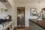 A traditional-style kitchen in a single-family home, looking between a gas range and a large wood island into a framed doorway that leads to a butler’s pantry, with abundant cabinets and a black and white checkered floor.