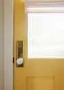 A close up image of a yellow door with fluted glass window, a white round doorknob, and brass hardware.