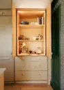 An image focusing on a light wood, floor to ceiling pantry cabinet or kitchen appliance garage with drawers and shelving.