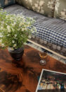 A vignette image of a coffee table in a living room, focused on colorful books, a vase full of small wildflowers, and a small drink in a coupe glass.