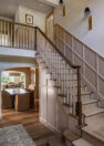 Looking into a traditional-style home, with a staircase on the right following the wall up to the second floor. The open stairway reveals the second floor at the top, where an open walkway is visible, as well a door to a bedroom at the top of the stairs. On the first floor, the formal dining room can be seen beyond the stairs.