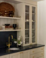 A living room hospitality bar with display cabinets, a black countertop, and a small sink. Serene Modern Tudor — Board & Vellum
