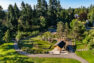 An aerial photograph of a public park showing the paved trail system, a play area, picnic area, and basketball court. The park is surrounded by large, established, evergreen trees.