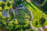 An aerial view of the public park, Westside Park, showing the new play area, walking path, pickleball court, and covered picnic area. The park is surrounded by an established wood which connects to an existing trail network.